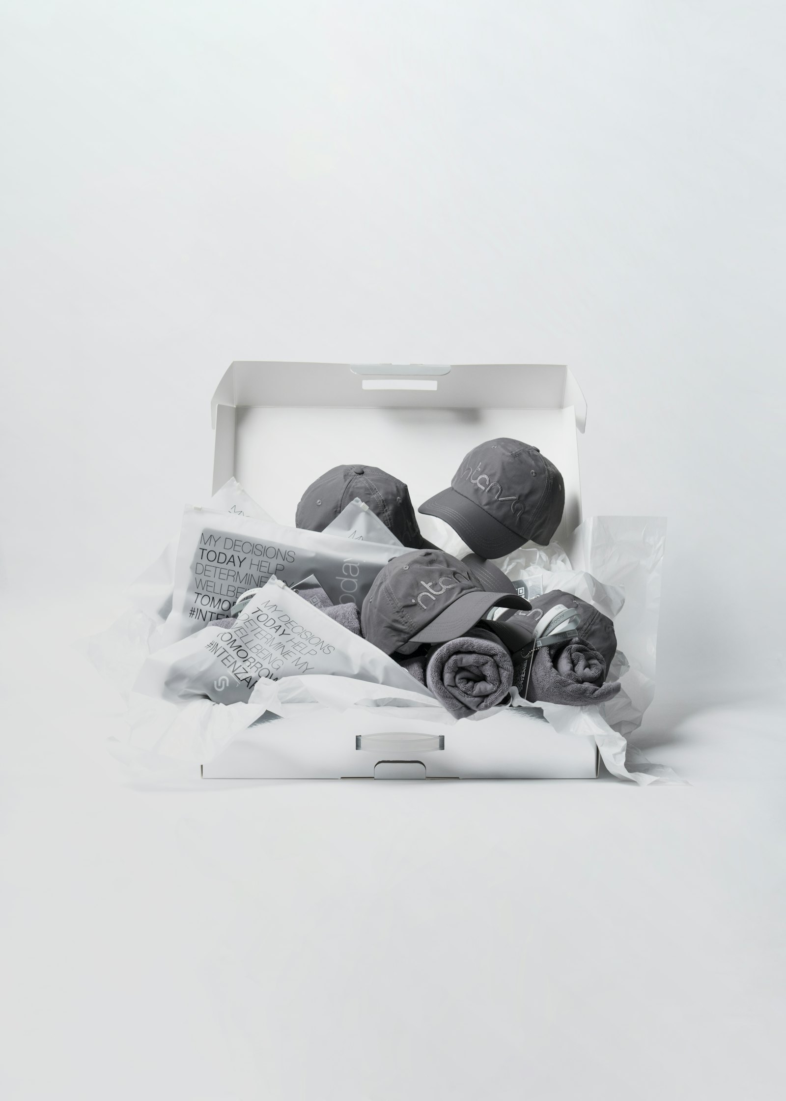An open gift box holding a folded cap, rolled textile and tissue paper.